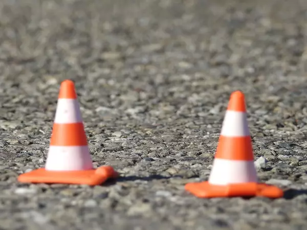 Im Vordergrund stehen zwei orange-weiss gestreifte Pylone auf grauem Asphalt.