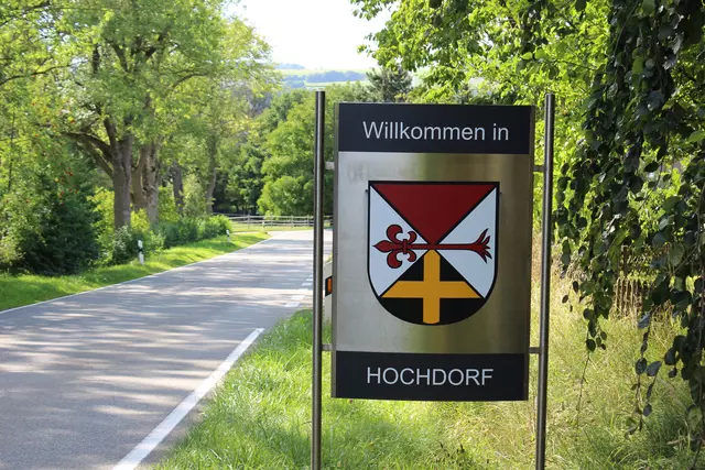 Willkommensschild mit dem Wappen der Gemeinde neben einer Straße.